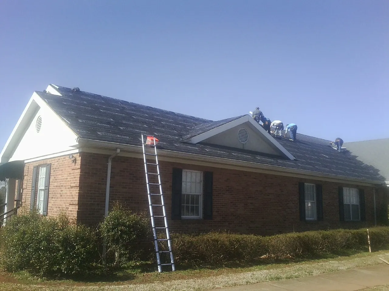 Crew tearing shingles off a brick ranch roof with a ladder set — Emergency Roof Repair work by our crew in Chicora