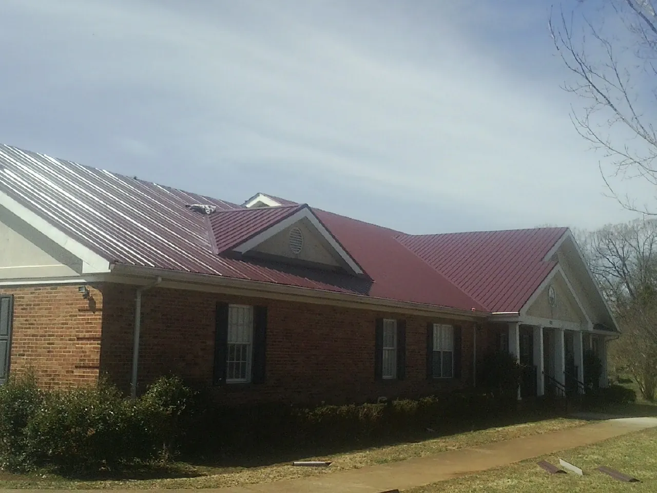 Red metal roof with gabled entries on a long brick building, from a Hail Damage Roof Repair job in Chicora