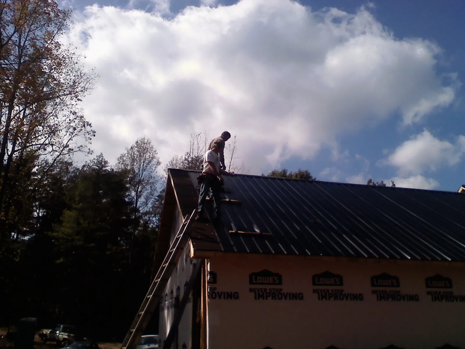 Roofer fastening dark metal panels high against a cloudy sky, from a Roof Inspection job in Chicora