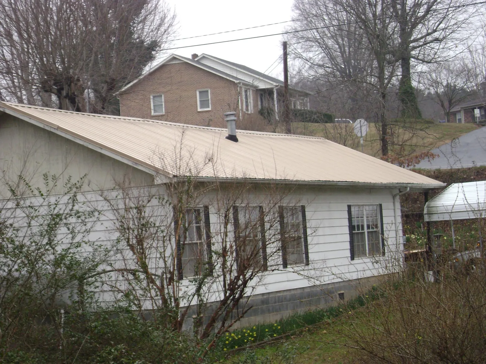 Tan metal roof on a white sided house set into a hillside — Commercial Roofing by Roofing Brothers in Chicora