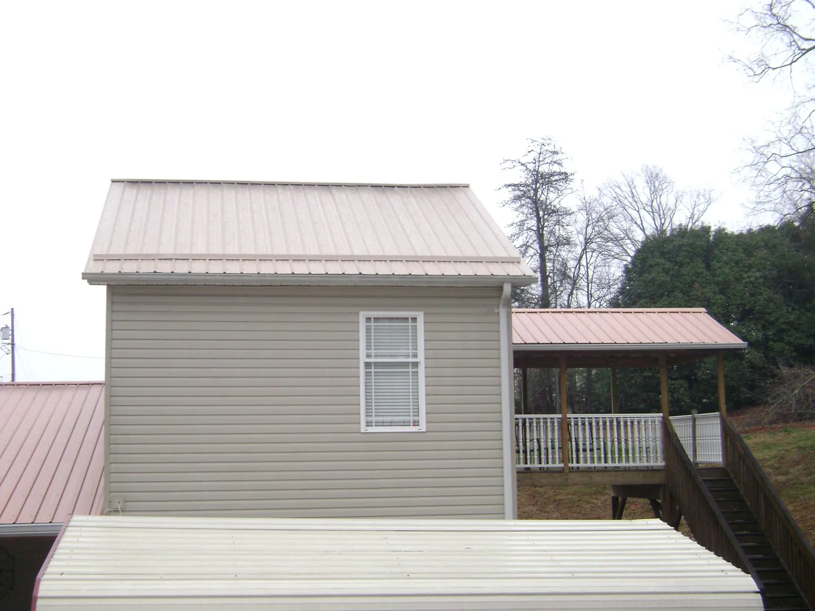 Tan metal roofs on a two story addition and attached porch, from a Roof Replacement job in Chicora